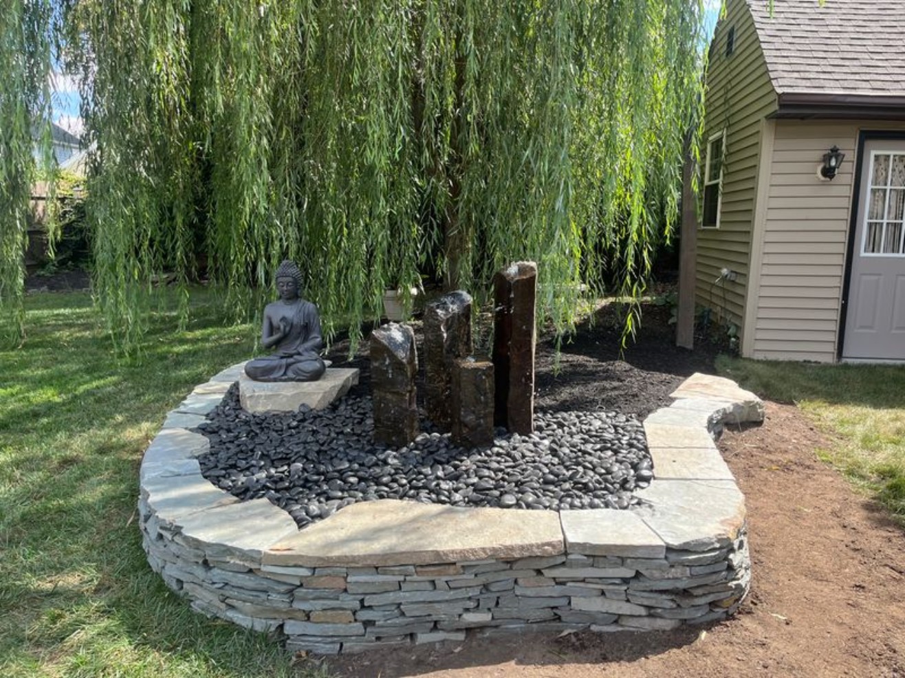 Basalt column fountain with Buddha statue beneath a weeping willow by AquaReale Philadelphia
