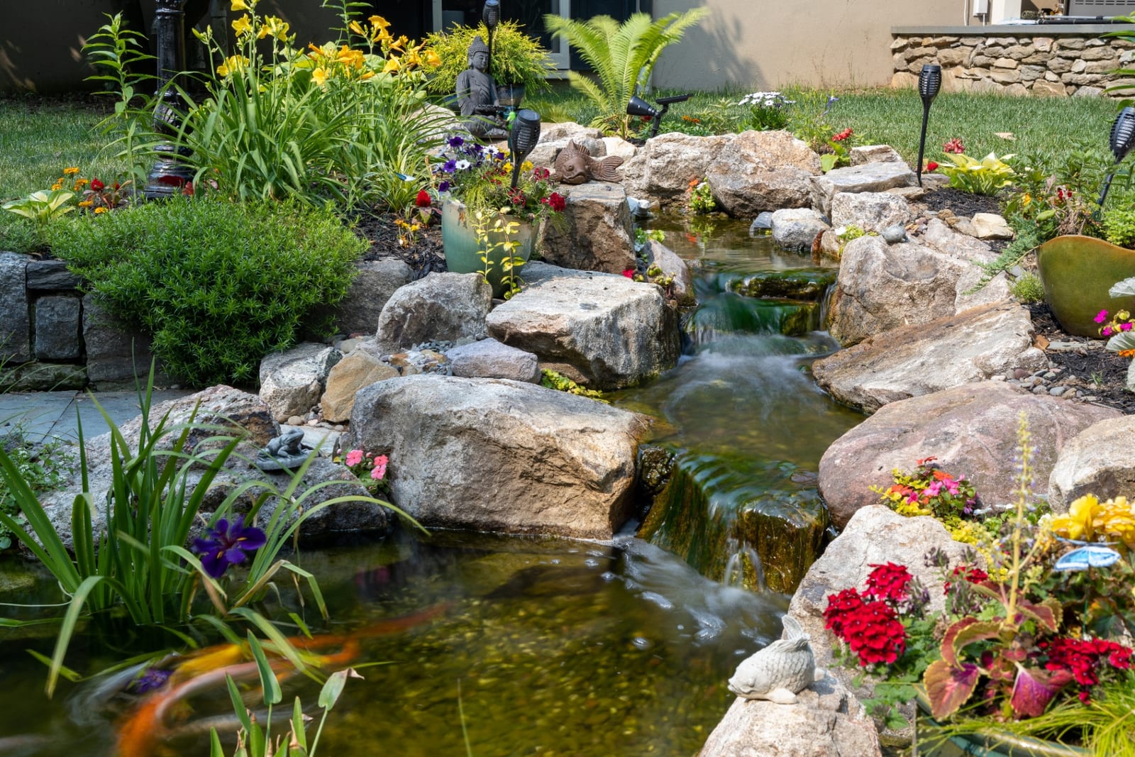 Koi stream with dense flowering borders and natural boulders by AquaReale Philadelphia