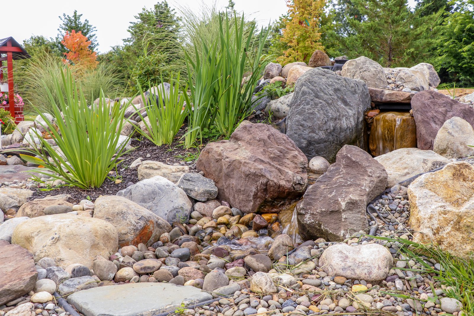 Disappearing waterfall with large boulders, river rock basin and ornamental grasses by AquaReale Philadelphia
