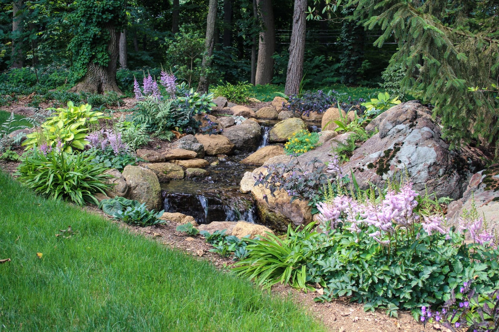 Disappearing waterfall stream bordered by lawn and flowering perennials by AquaReale Philadelphia
