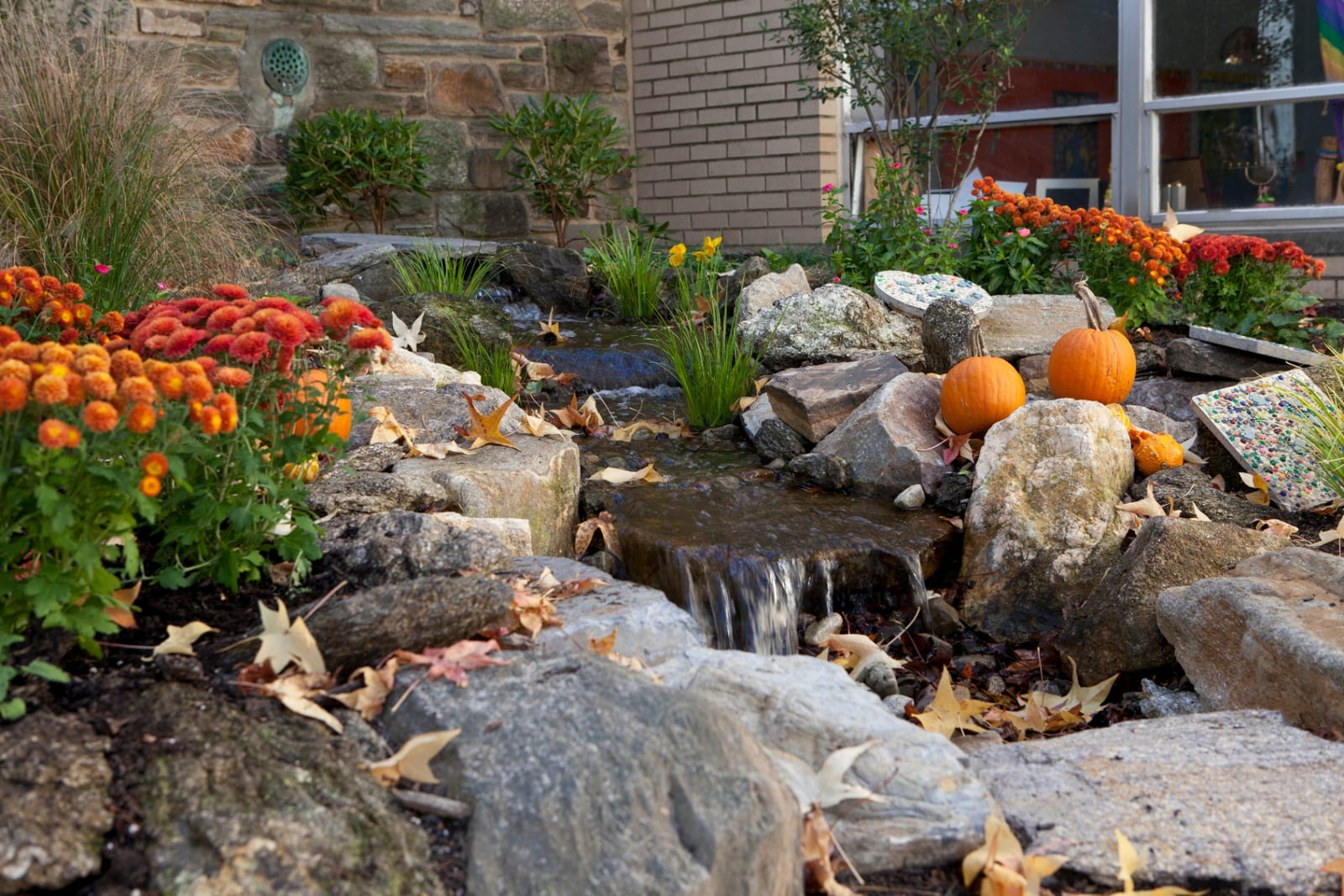 Disappearing waterfall with autumn mums and pumpkins beside a stone building by AquaReale Philadelphia