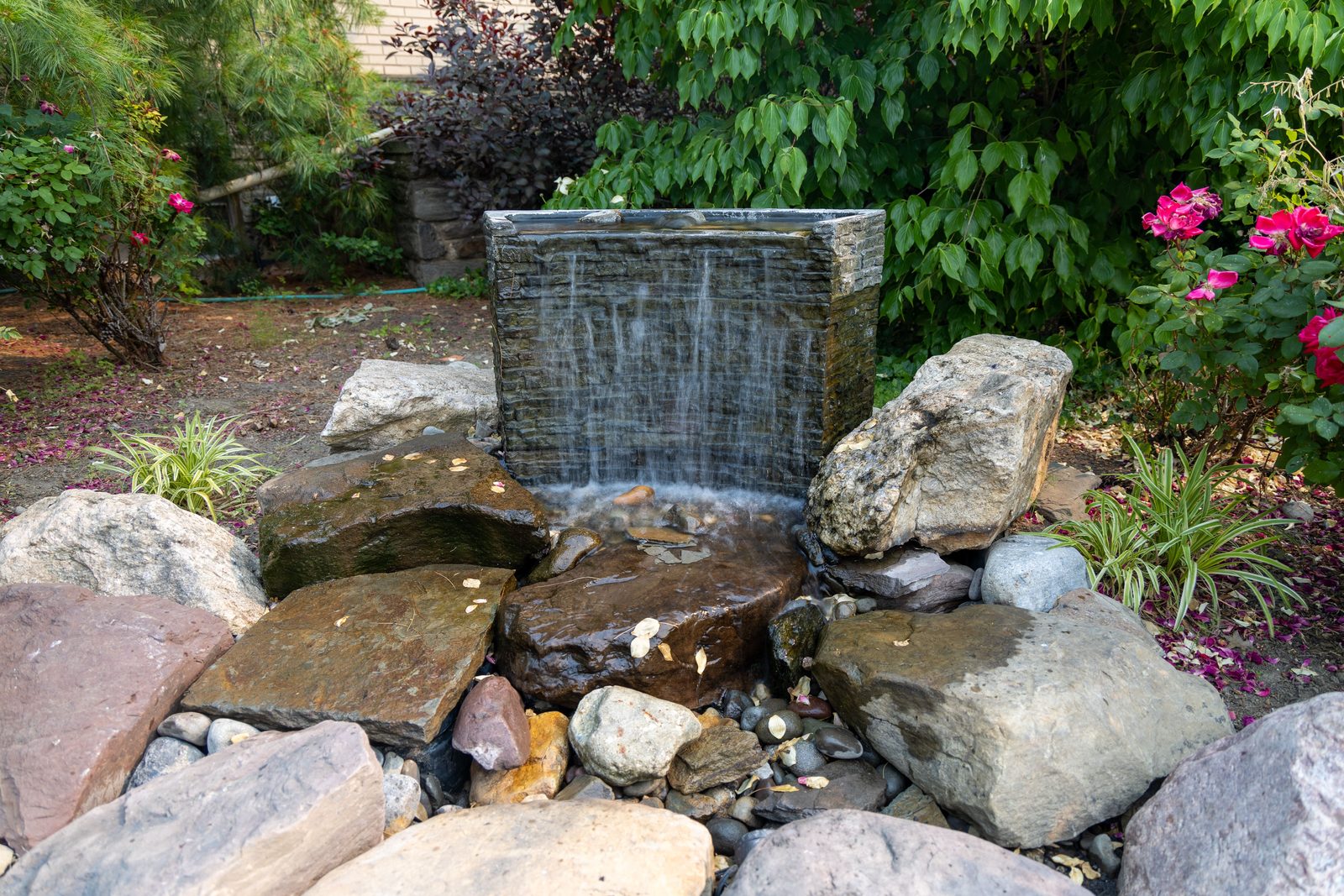 Slate water wall spilling over natural boulders into a river rock bed by AquaReale Philadelphia