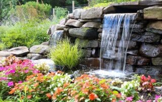 Garden waterfall with colorful flowers and rocks.
