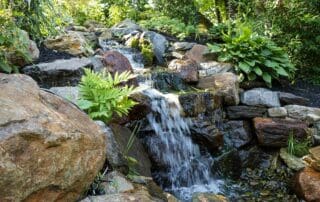 Tranquil garden waterfall over rocks with green foliage.