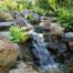 Tranquil garden waterfall over rocks with green foliage.